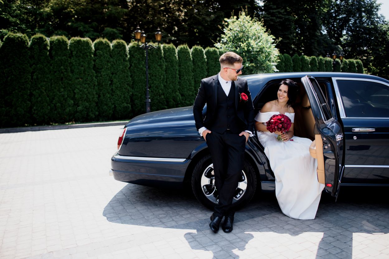 Beautiful wedding couple arriving in luxury limo service with professional chauffeur transportation